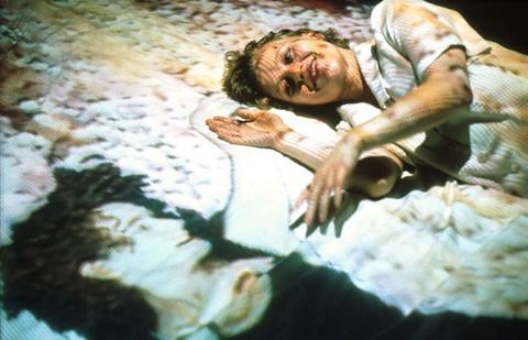 Image of Paul Sermon's Telematic Dreaming, a woman lying on a bed reaching out to another woman projected on the other side of the bed, both women are looking at each other