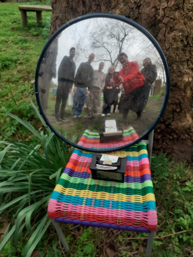 reflection of people looking into a circular fish eye mirror, sitting on a chair below a tree with a small printer in front of the mirror