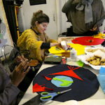 People sitting around the table making an artwork from brightly coloured felt, with plates for biscuits, scissors and glue on the table.