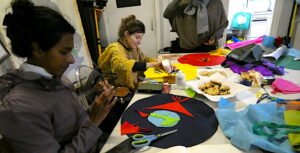People sitting around the table making an artwork from brightly coloured felt, with plates for biscuits, scissors and glue on the table.