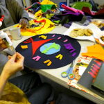 People sitting around the table making an artwork from brightly coloured felt, with plates for biscuits, scissors and glue on the table.
