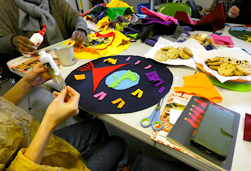 People sitting around the table making an artwork from brightly coloured felt, with plates for biscuits, scissors and glue on the table.