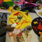 People sitting around the table making an artwork from brightly coloured felt, with plates for biscuits, scissors and glue on the table.