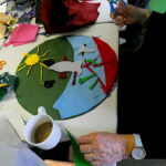 People sitting around the table making an artwork from brightly coloured felt, with plates for biscuits, scissors and glue on the table.