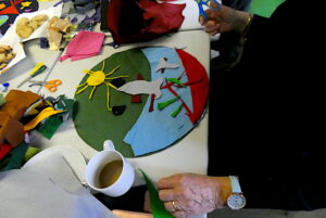 People sitting around the table making an artwork from brightly coloured felt, with plates for biscuits, scissors and glue on the table.
