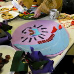 A circular artwork madefrom brightly coloured felt, with plates for biscuits, scissors and glue on the table.