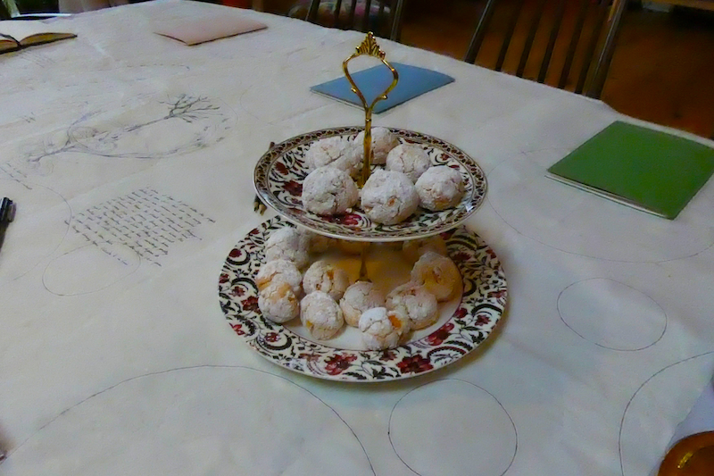 biscuits on a cake stand in the centre of a table cloth with drawings and writing on it and notebooks laid out at each place setting