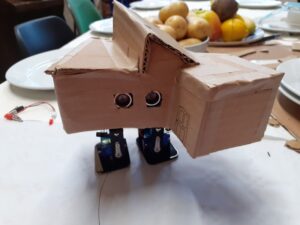A robot house with legs and chicken feet on a table with autumnal fruit in the background