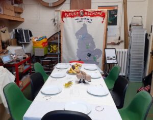 The first kinship table set up at Primary Studios with the dancing house robot and the crazy robot dog on the table and the Future Machine banner behind the table.