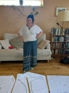 Rachel standing with hands on her hips in the gathering space with a sofa behind her and pieces of cloth on the floor in front of her