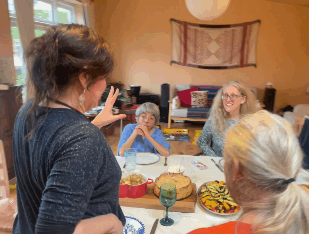 Rachel talking with food laid on the table and people sitting around it