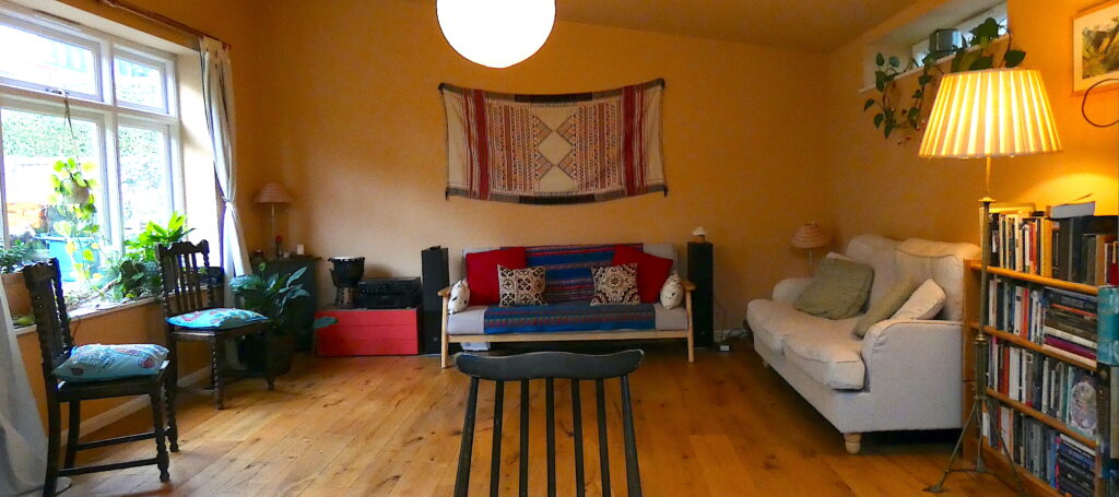 A spacious room with wooden floors, chairs and sofas against the walls and light coming through the window