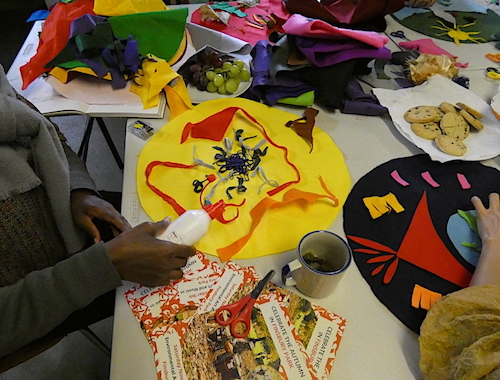 People sitting around the table making an artwork from brightly coloured felt, with plates for biscuits, scissors and glue on the table.