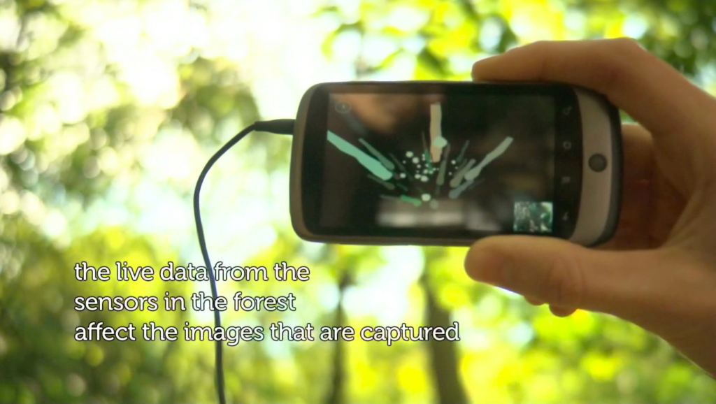A mobile phone held up against light appearing through trees with a visualisation of weather data and a small image taken by the phone appearing on the screen.