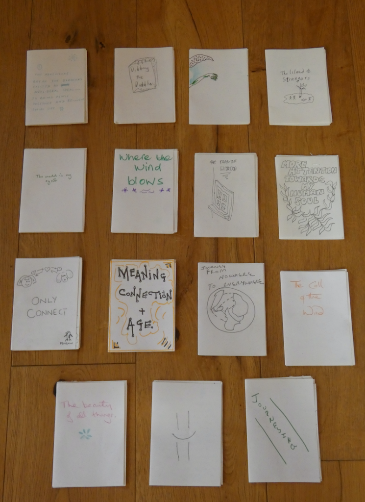 15 small handmade books laid out on a wooden floor.
