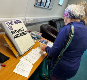 A woman looking at the Book of Rituals and Robots and small booklets with the stories from a previous workshop